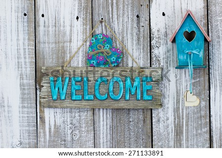 Antique teal blue welcome sign with heart by birdhouse hanging on white painted weathered wood fence