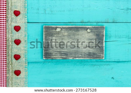 Blank rustic wood sign on antique teal blue wooden background with red and white gingham, burlap and rope border with red hearts