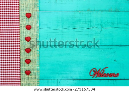 Welcome sign on antique teal blue wooden background with red and white checkered fabric, burlap and rope border with red hearts