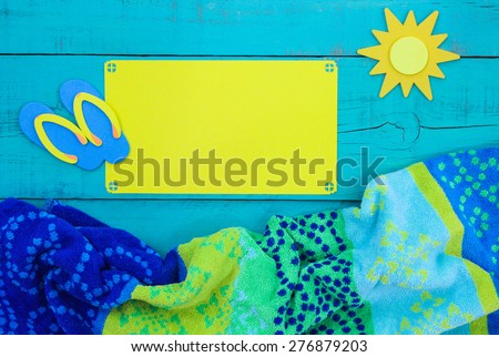 Blank bright yellow sign and sun on teal blue wooden background with beach towel and sandals border