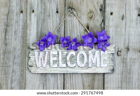 Rustic welcome sign with purple balloon flowers hanging on weathered wooden background