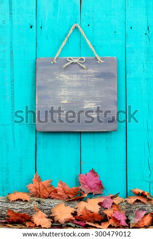 Rustic blank sign hanging on teal blue wood background over log covered in fall leaves
