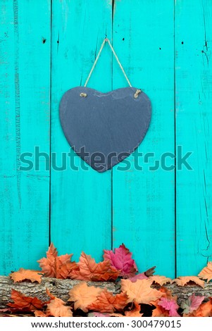 Slate heart hanging on rustic teal blue wood background by log covered in fall leaves border