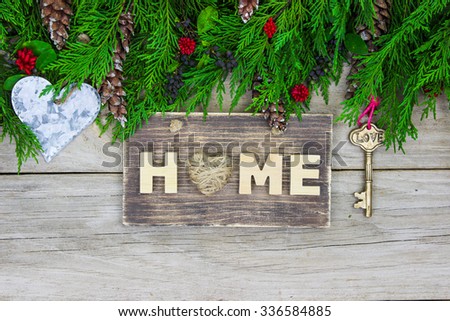 Home sign with green garland border, tin heart and brass skeleton key on antique rustic wood background