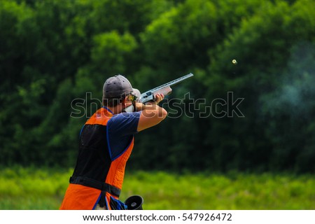 Young man skeet shooting outdoors; shooting clay pigeon targets at gun club with airborne casing and copy space