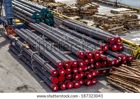 A pile of round and square metal pipes, chocks , packed in stacks with tags size parameters for cranes and transport of cargo ships in the seaport and railway wagons