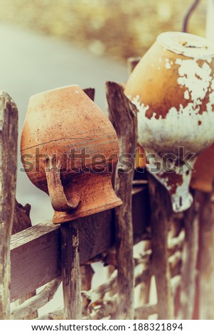 Related structure twigs and sticks in a vintage wooden rural fence with creative household items - old clay pots for cooking as trendy abstract background for design
