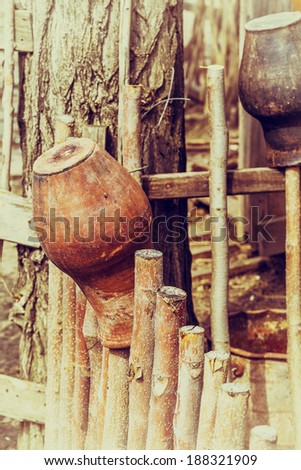 Related structure twigs and sticks in a vintage wooden rural fence with creative household items - old clay pots for cooking as trendy abstract background for design