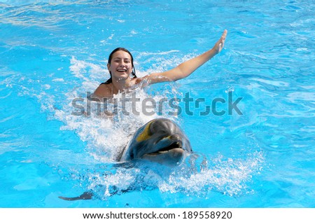 Beautiful young happy girl laughs and swims with dolphins in the blue dolphin pool lesson