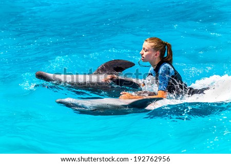 A young girl trains Glad beautiful dolphin in blue water in the pool on a bright sunny day on the original submission for tourists