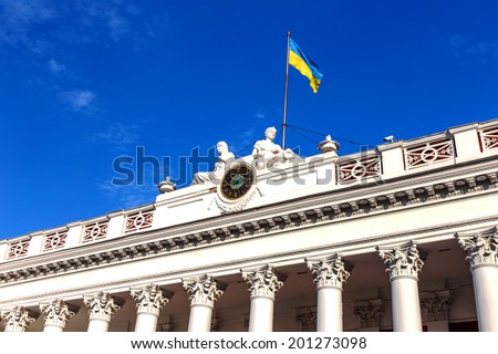 facade of the building official Odessa City Hall with the city\'s main clock and the Ukrainian flag on a background of bright blue sky
