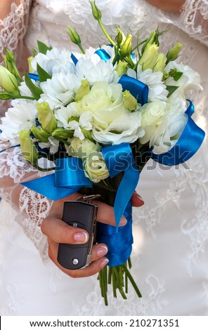 Beautiful wedding bouquet in hands of the bride and wedding gift keychain alarm on a new car