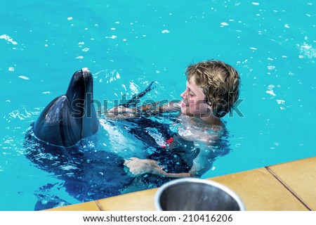 Happy handsome young boy laughing and swimming with dolphins in the blue swimming pool on a bright sunny day on the occupation of the dolphin