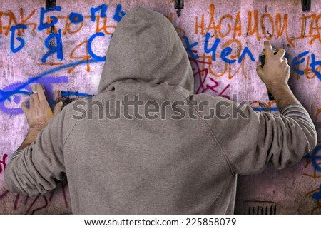 Graffiti artist in a gray dress with a hood spray paint for a picture on the wall of the urban culture. Beautiful street art graffiti. Urban Contemporary Culture. Isolated on white background