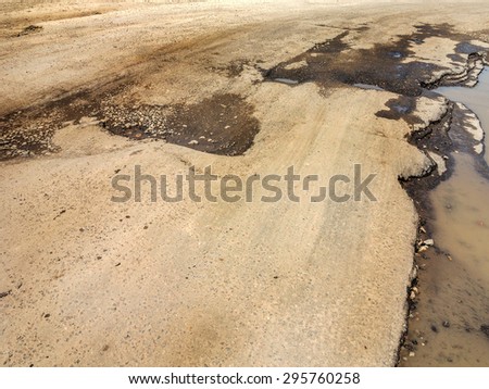 Damaged asphalt road with potholes caused by freezing and thawing cycles during the winter. Poor road.