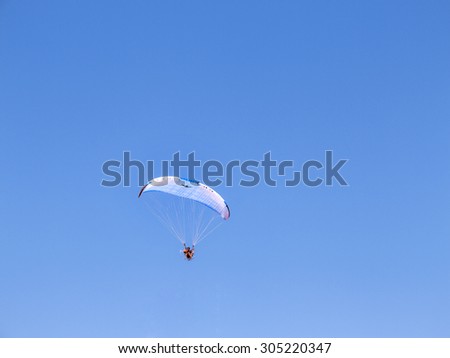 Odessa, Ukraine August 8, 2015: aredevil pilot with a motorized glider flying fast in the blue sky over the seaside with leisure travelers on the beach. airplane