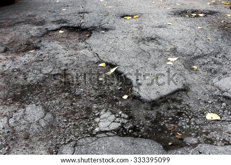 The damaged asphalt road with potholes caused by freeze-thaw cycles during winter. Bad road. Road repair