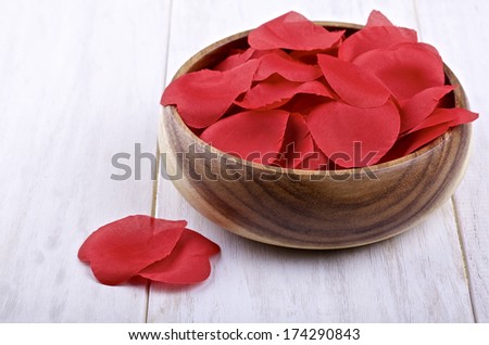 Artificial petals of roses in a wooden container on painted a light background
