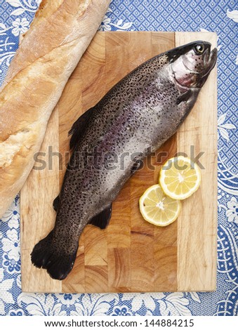 freshly caught trout, served on a wooden plank, served with bread and slices of lemon, close up, white tablecloth with blue pattern
