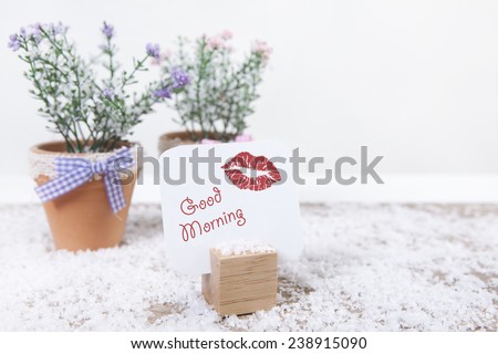 on a table with flowers is a sign with the text good morning