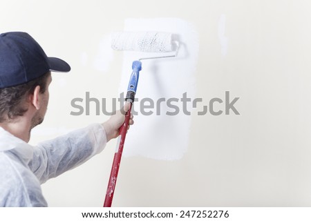 Painter paints an old wall with a paint roller in white