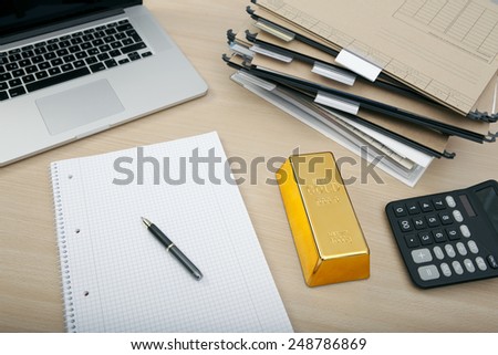 in an office at a desk with laptop and calculator is a gold bar
