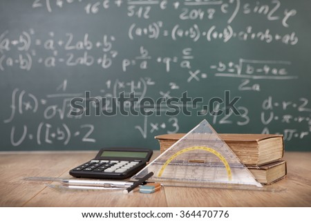 Schoolbooks and calculator lying on a wooden school desk in front of a green chalkboard with Mathematical formulas school