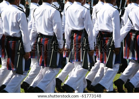 Soldiers wearing parade army wear.  They are marching at a formal ceremony.  These uniforms are white with a patterned wrap around on the waist.  Celebrations of the Sultan of Brunei\'s birthday.