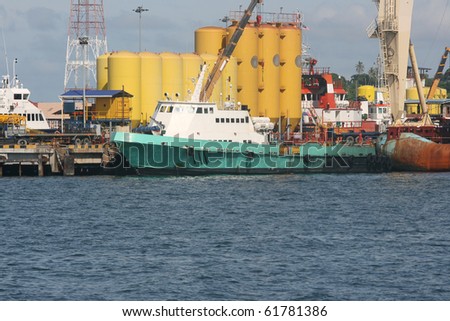 Busy dock scene, with boats, industrial buildings and cranes.