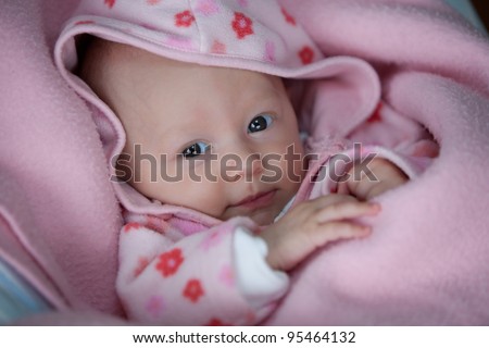 A young baby girl snuggled up in pink blankets