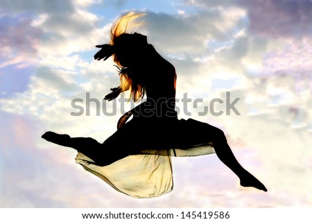 A silhouette of a young, attractive, dancing woman jumps through the air, with a beautiful cloudy sunset in the background outside.