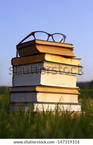a pair of thick black women\'s eyeglasses sit on top of a stack of thick old books, Bibles, and hymnals outside.