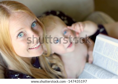 An attractive, smiling young Christian woman is reading the book, the Holy Bible while her baby boy sits on her lap.