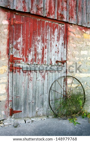 a rustic old wooden barn door with peeling red paint, stone walls, and a rusted antique wagon wheel at a Midwestern farm.