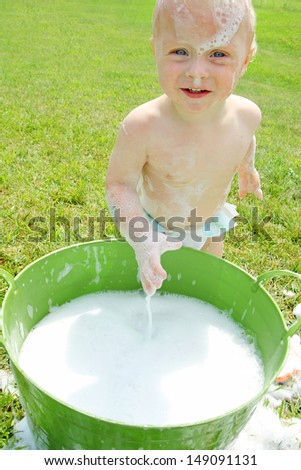 a baby is splashing around outside in a bucket full of soap bubbles and water on a summer day
