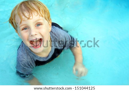 a cute, happy child is smiling as he looks up at the camera and jumps around in a swimming pool on a hot summer day.  Empty Room on Water for text / copy space.