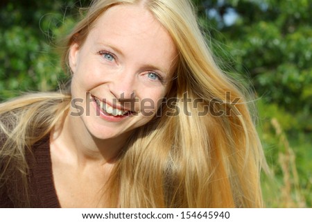 a young, attractive, 30 year old Caucasian woman is sitting outside in nature, with her silky long blonde hair blowing in the wind
