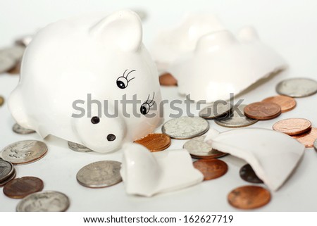 a small white piggy bank has just been broken into pieces and coin money is lying scattered around it, isolated on a white background