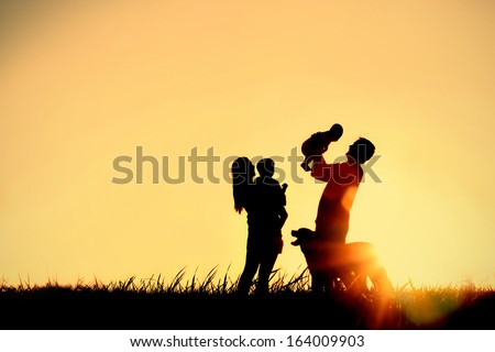 A silhouette of a happy family of four people, mother, father, baby, and child, and their dog in front of a sunsetting sky, with room for copy space or text