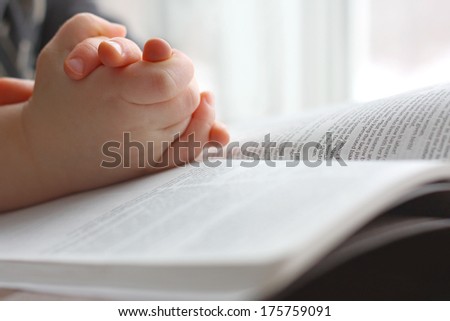 the hands of a young Christian child are folded in prayer over the book the Holy Bible