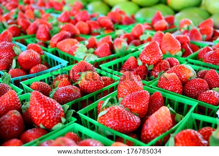 a collection of fresh strawberries are gathered in baskets on a sale table at a farmer\'s market.