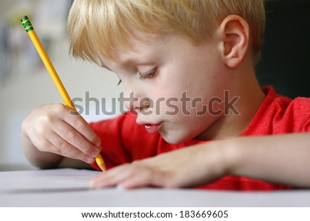 a cute young child is making a funny face as he is working at drawing on paper with a pencil