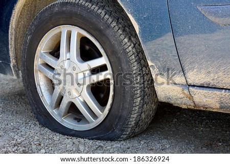close up on the flat tire of a dirty old blue car stranded on a gravel road