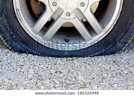 a close up, centered view of a flat car tire that has popped on a gravel road.  Room for copy-space.
