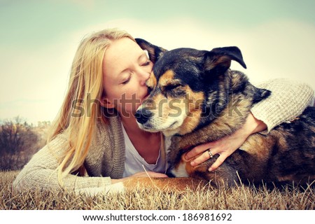Young woman and her German Shepherd dog lying in the grass, she is hugging and kissing him. Vintage style color.