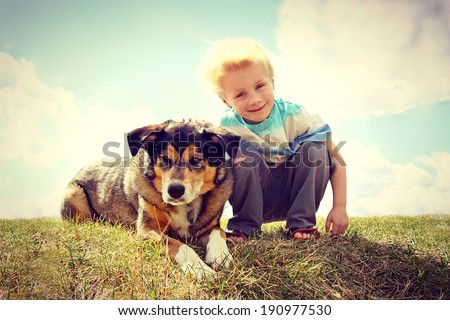 a young boy child is sitting outside in the grass, smiling as he pets his German Shepherd Dog.  VIntage Style Color.