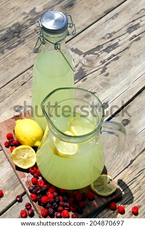 Two pitchers of fresh squeezed lemonade are sitting outside on a rustic wood picnic table surrounded by Raspberry fruit on a summer day,