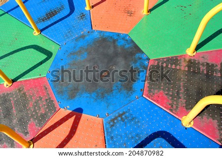 A close up of an old, vintage, metal, rainbow colored piece of children\'s playground equipment called a merry-go round or roundabout.