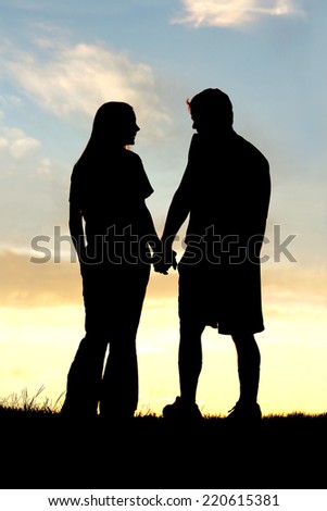A silhouette of a happy young couple in a relationship, holding hands and talking as they walk outside at sunset.