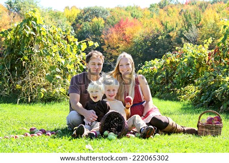a happy family of four attractive caucasian people is sitting in an apple orchard in the Autumn forest, eating a fresh fruit picnic